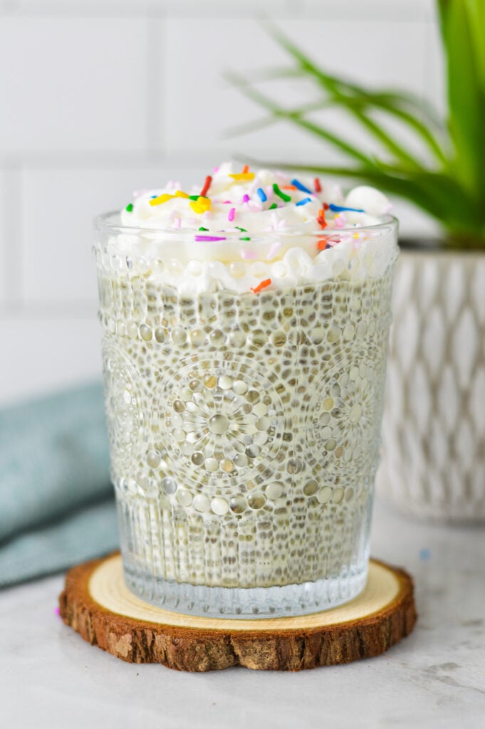 A glass cup filled with Birthday Cake Chia Pudding, topped with whipped cream and candy sprinkles.