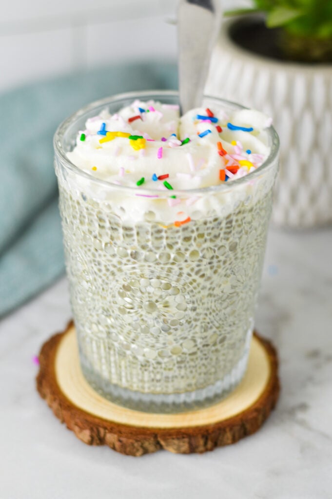 Birthday Cake Chia Pudding in a small glass cup, topped with homemade whipped cream and rainbow sprinkles.