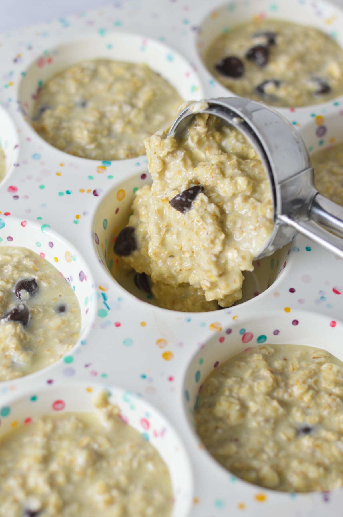 A medium cookie scoop scooping some Chocolate Chip Baked Oatmeal Cup batter into a silicone muffin pan.