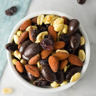 A small ramekin filled with Cranberry Chocolate Almond Trail Mix, with a mix of dried cranberries, dry roasted peanuts and whole almonds.