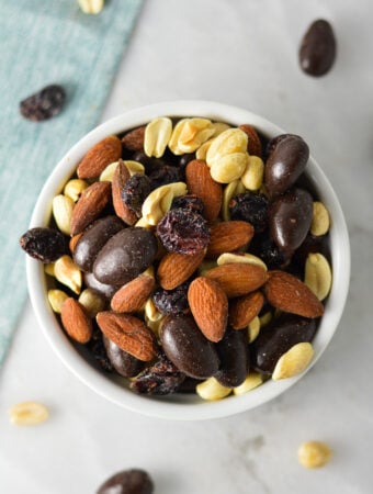 A small ramekin filled with Cranberry Chocolate Almond Trail Mix, with a mix of dried cranberries, dry roasted peanuts and whole almonds.
