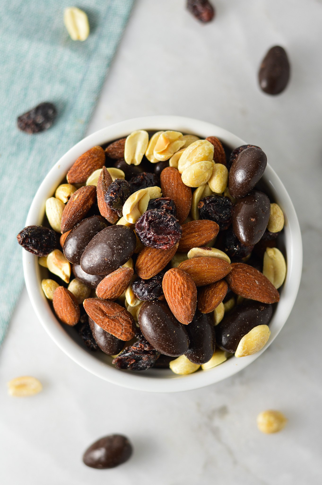 A small ramekin filled with Cranberry Chocolate Almond Trail Mix, with a mix of dried cranberries, dry roasted peanuts and whole almonds.