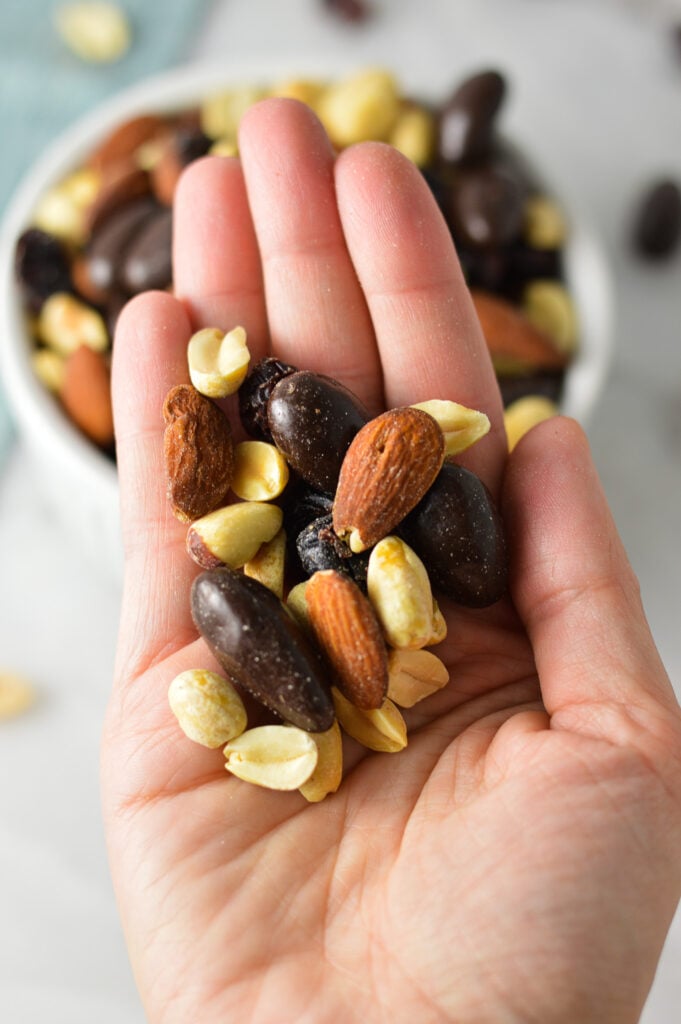 A hand holding a handful of Cranberry Chocolate Almond Trail Mix, clearly showing the crunchy texture of the mix.