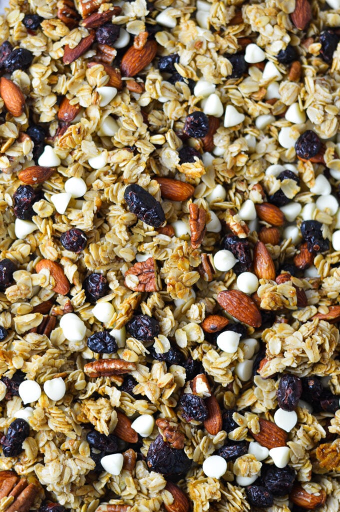 A sheet pan filled with Cranberry White Chocolate Granola, with white chocolate chips, almonds, whole pecans and dried cranberries dispersed in the freshly baked granola.