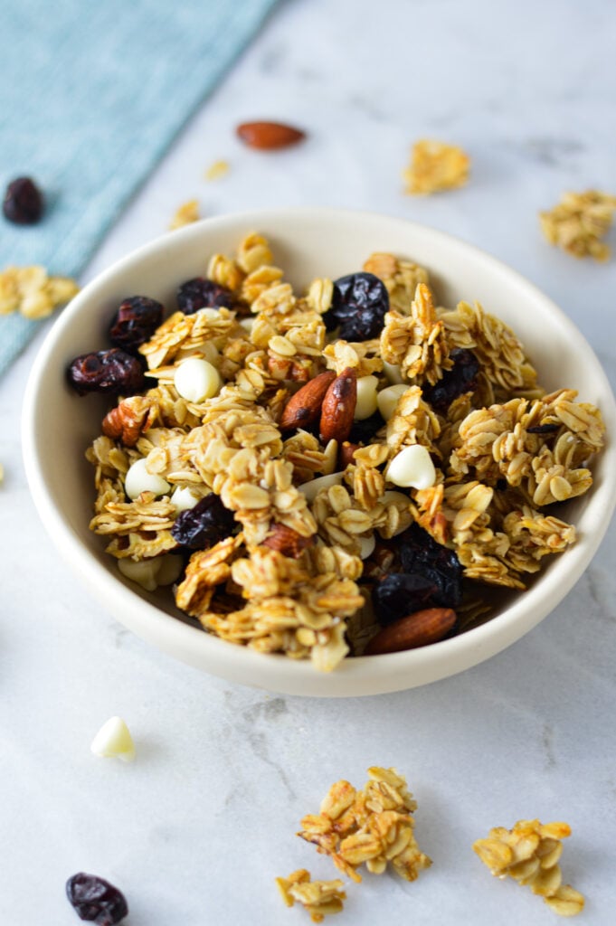A bowl full of Cranberry White Chocolate Granola, with some granola clusters on the granite surface in the background.