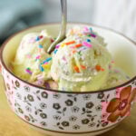 A small bowl filled with homemade Ninja Creami Birthday Cake Ice Cream, with a small spoon sticking out of the creamy ice cream.
