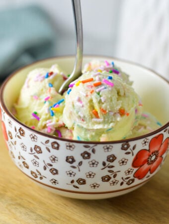 A small bowl filled with homemade Ninja Creami Birthday Cake Ice Cream, with a small spoon sticking out of the creamy ice cream.