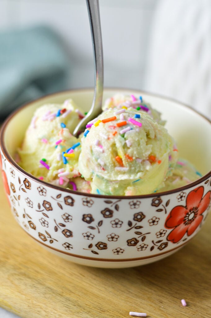 A small bowl filled with homemade Ninja Creami Birthday Cake Ice Cream, with a small spoon sticking out of the creamy ice cream.