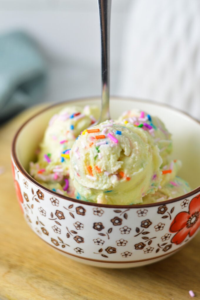 A bowl full of colorful Ninja Creami Birthday Cake Ice Cream, with a metal spoon sticking out of the bowl full of ice cream.