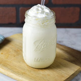 Homemade Ninja Creami Vanilla Bean Milkshake on a wooden surface, with a clear straw coming out of the creamy milkshake.