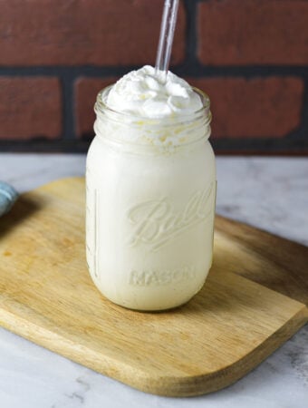 Homemade Ninja Creami Vanilla Bean Milkshake on a wooden surface, with a clear straw coming out of the creamy milkshake.
