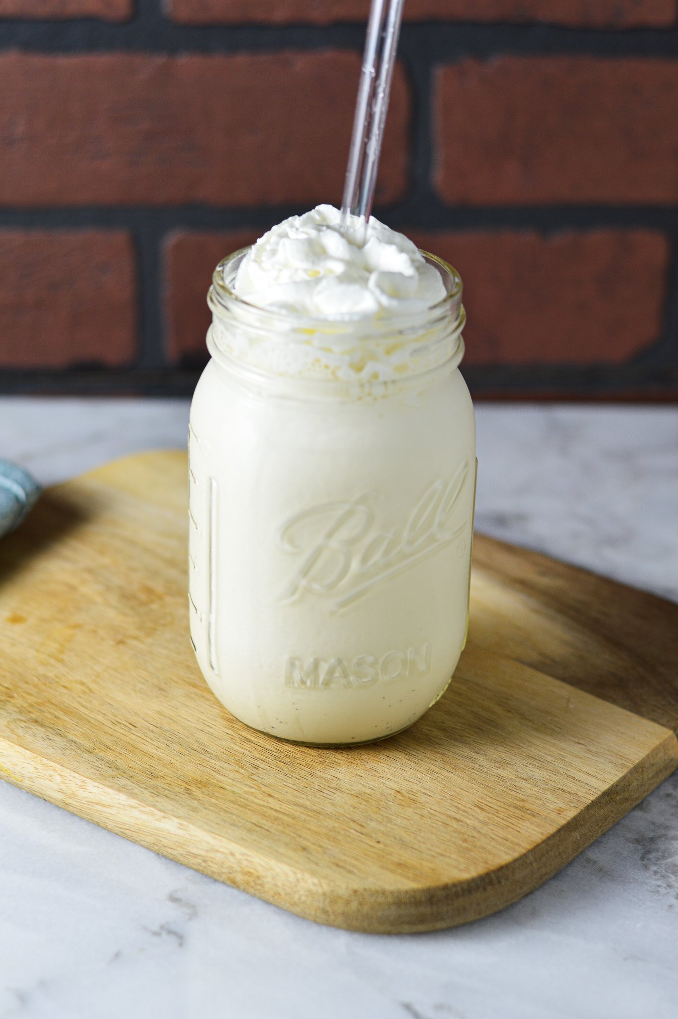 Homemade Ninja Creami Vanilla Bean Milkshake on a wooden surface, with a clear straw coming out of the creamy milkshake.