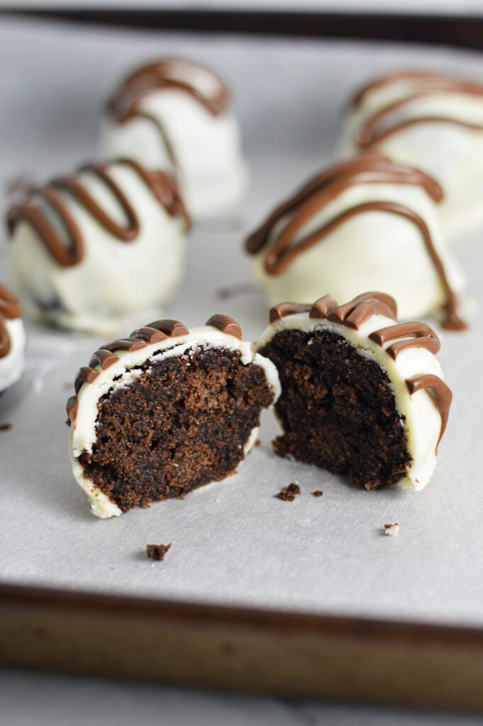 Some Nutella White Chocolate Cake Balls on a parchment paper lined baking sheet, with the front Nutella ball cut in half showing the dense fudgy inside.