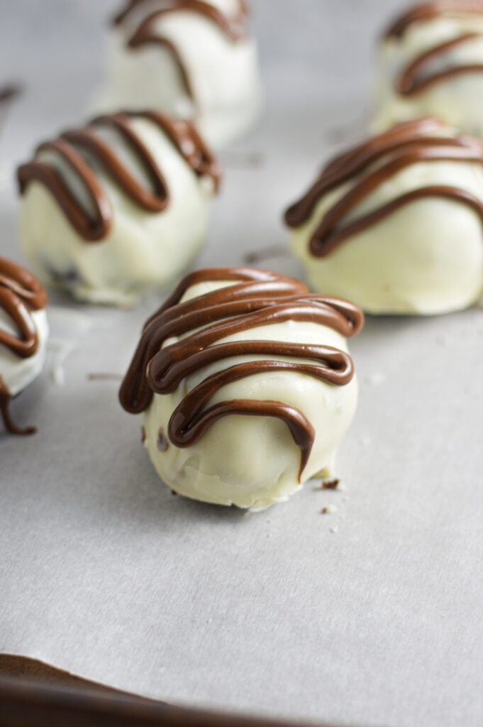 Nutella White Chocolate Cake Balls on a parchment paper lined cookie sheet, with a drizzle of Nutella on top of the white chocolate balls.
