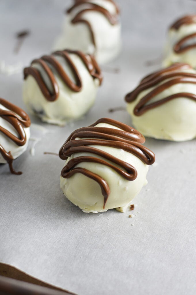Nutella White Chocolate Cake Balls on a parchment paper lined cookie tray, with chocolate drizzle on top of each white chocolate cake ball.