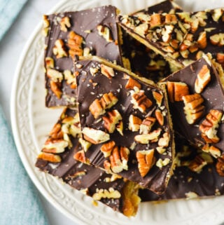 A small plate with some homemade Saltine Cracker Toffee, with the melted chocolate chips topped with chopped pieces of pecan.