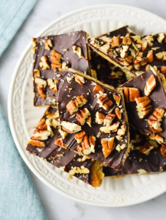 A small plate with some homemade Saltine Cracker Toffee, with the melted chocolate chips topped with chopped pieces of pecan.