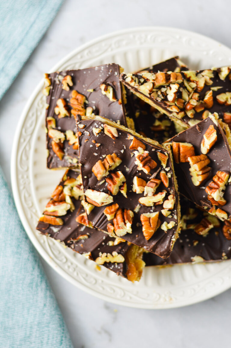 A small plate with some homemade Saltine Cracker Toffee, with the melted chocolate chips topped with chopped pieces of pecan.