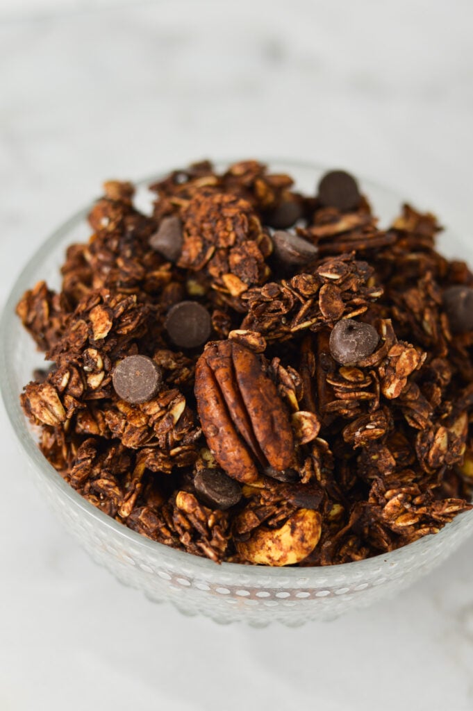 A glass bowl full of Chocolate granola made with rolled oats, roasted pecans and rich chocolate chips.