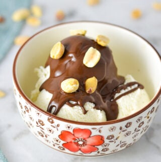 A small bowl with vanilla ice cream topped with Chocolate Peanut Butter Magic Shell and topped with oven roasted peanuts.