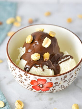 A small bowl with vanilla ice cream topped with Chocolate Peanut Butter Magic Shell and topped with oven roasted peanuts.