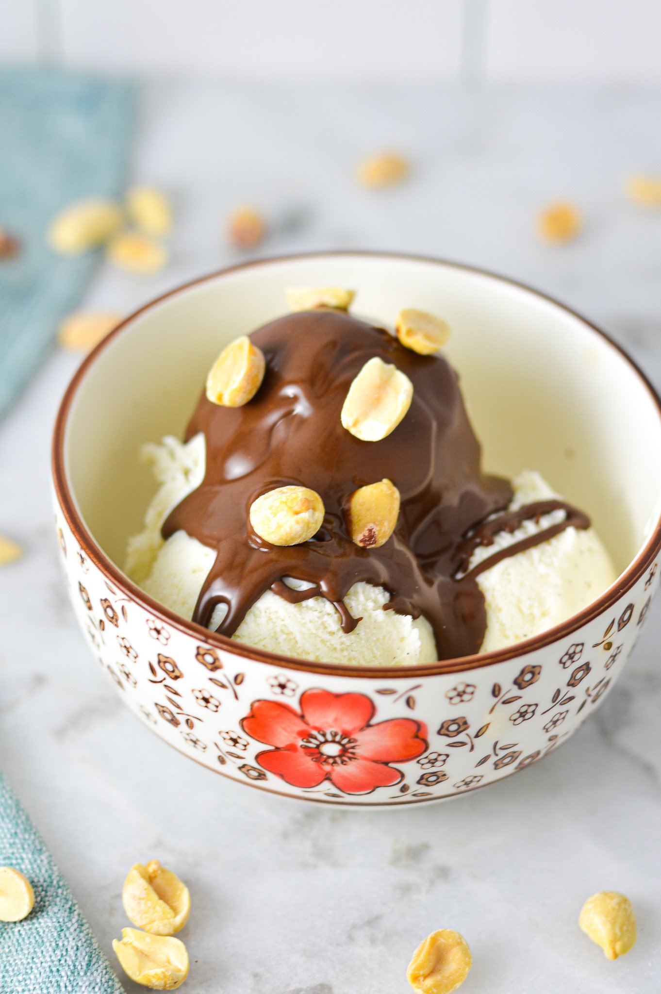 A small bowl with vanilla ice cream topped with Chocolate Peanut Butter Magic Shell and topped with oven roasted peanuts.