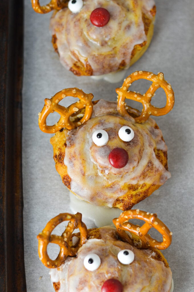 A parchment paper lined cookie sheet with Easy Reindeer Cinnamon Rolls on top: premade cinnamon rolls made to look like Rudolph the red nosed reindeer.