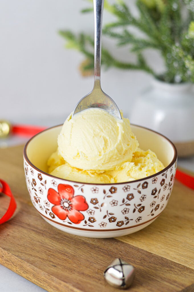 A small bowl full of Ninja Creami Eggnog Ice Cream, with a spoon sticking out of the creamy dessert.