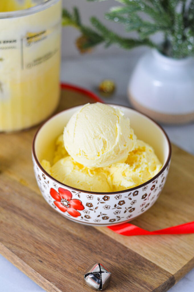 A small bowl full of Ninja Creami Eggnog Ice Cream, with a Ninja Creami Pint container with leftover Ninja Creami ice cream in the background.