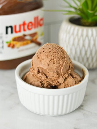 Homemade Ninja Creami Nutella Ice Cream in a small ramekin, with a jar of Nutella in the background.