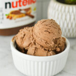 Scoops of Ninja Creami Nutella Ice Cream in a white ramekin, with a Nutella jar in the background.