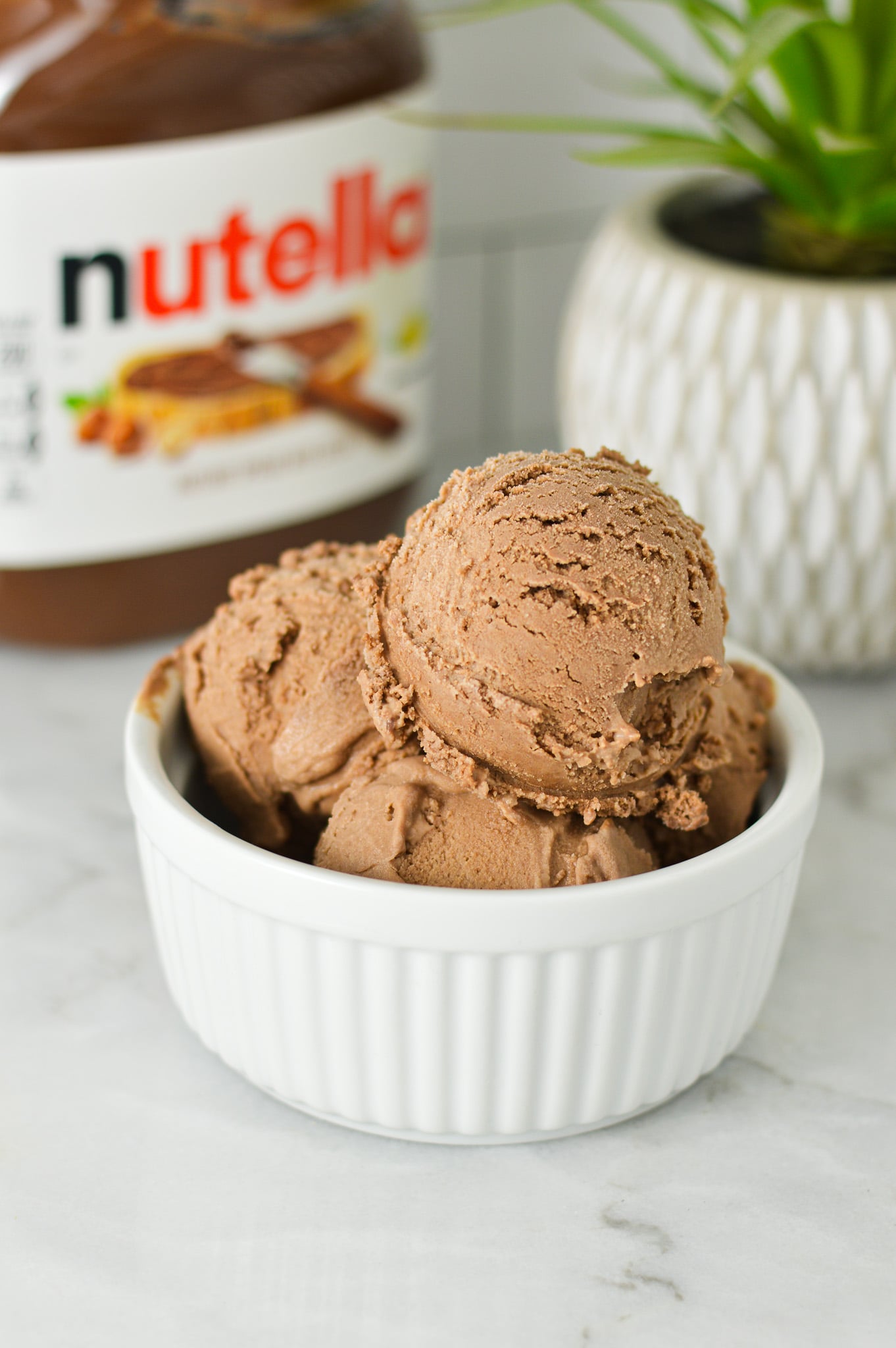 Scoops of Ninja Creami Nutella Ice Cream in a white ramekin, with a Nutella jar in the background.