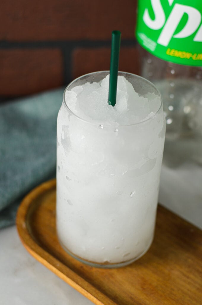 A highball glass filled with Ninja Creami Sprite Slushie, with a plastic straw in the refreshing drink.