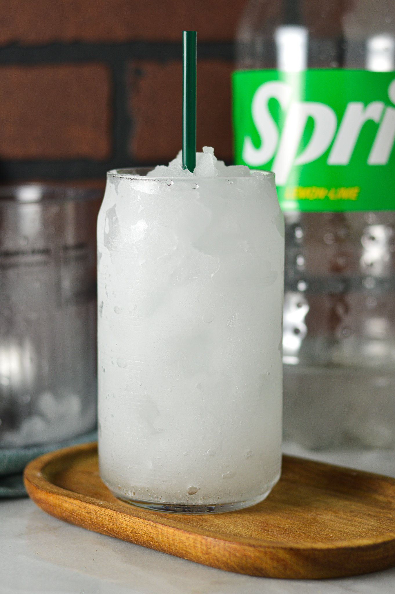 A clear glass filled with Ninja Creami Sprite Slushie, with a Ninja Creami pint container and a 2L bottle of Sprite in the background.