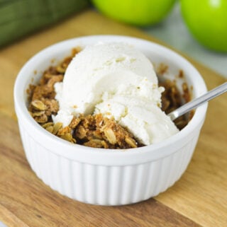A small ramekin filled with Apple Crisp for One, topped with a scoop of vanilla ice cream.