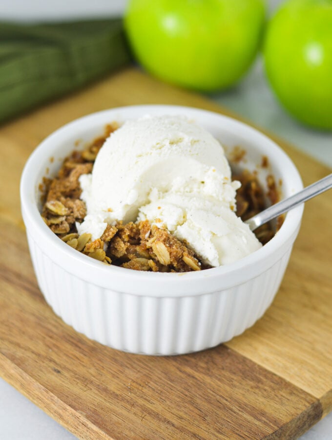 A small ramekin filled with Apple Crisp for One, topped with a scoop of vanilla ice cream.
