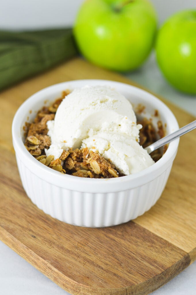 A small ramekin filled with Apple Crisp for One, topped with a scoop of vanilla ice cream.