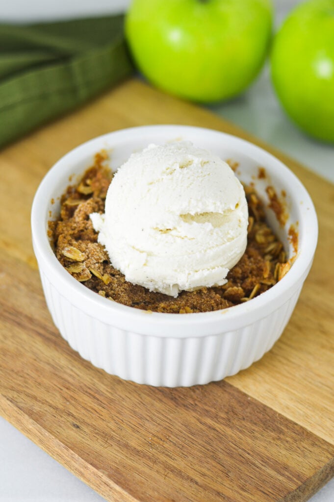 A small bowl filled with freshly baked Apple Crisp for One, topped with a scoop of vanilla bean ice cream.