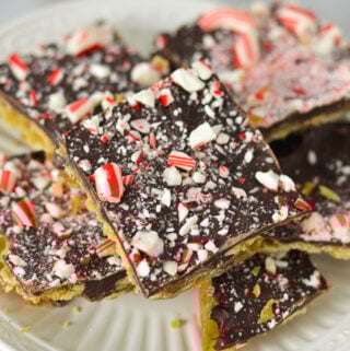 A small plate filled with Candy Cane Saltine Toffee, topped with crushed candy cane on top of the melted chcolate layer.