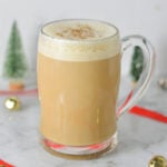 A clear mug full of Eggnog Latte, with the frothy milk topped with ground nutmeg.