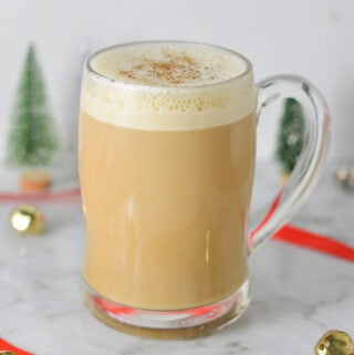 A clear mug full of Eggnog Latte, with the frothy milk topped with ground nutmeg.