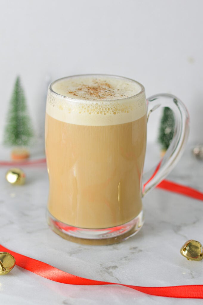 A clear mug full of Eggnog Latte, with the frothy milk topped with ground nutmeg.