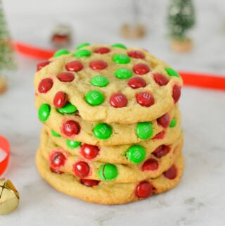 A stack of Mini M&M Christmas Cookies with red ribbon and silver and gold bells in the background, giving the scene a real holiday season feeling.