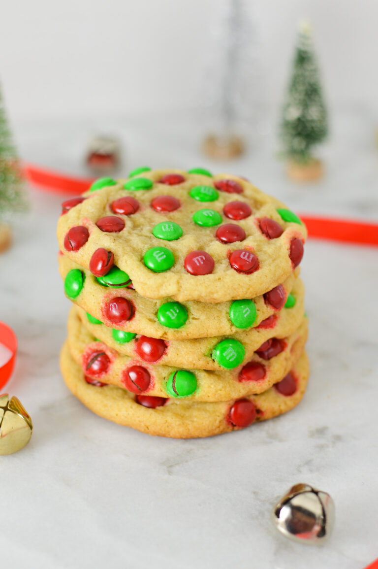 A stack of Mini M&M Christmas Cookies with red ribbon and silver and gold bells in the background, giving the scene a real holiday season feeling.