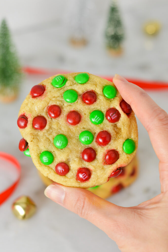 A hand holding up a Mini M&M Christmas Cookie, with the Christmas M&Ms dispersed evenly in the soft cookie.