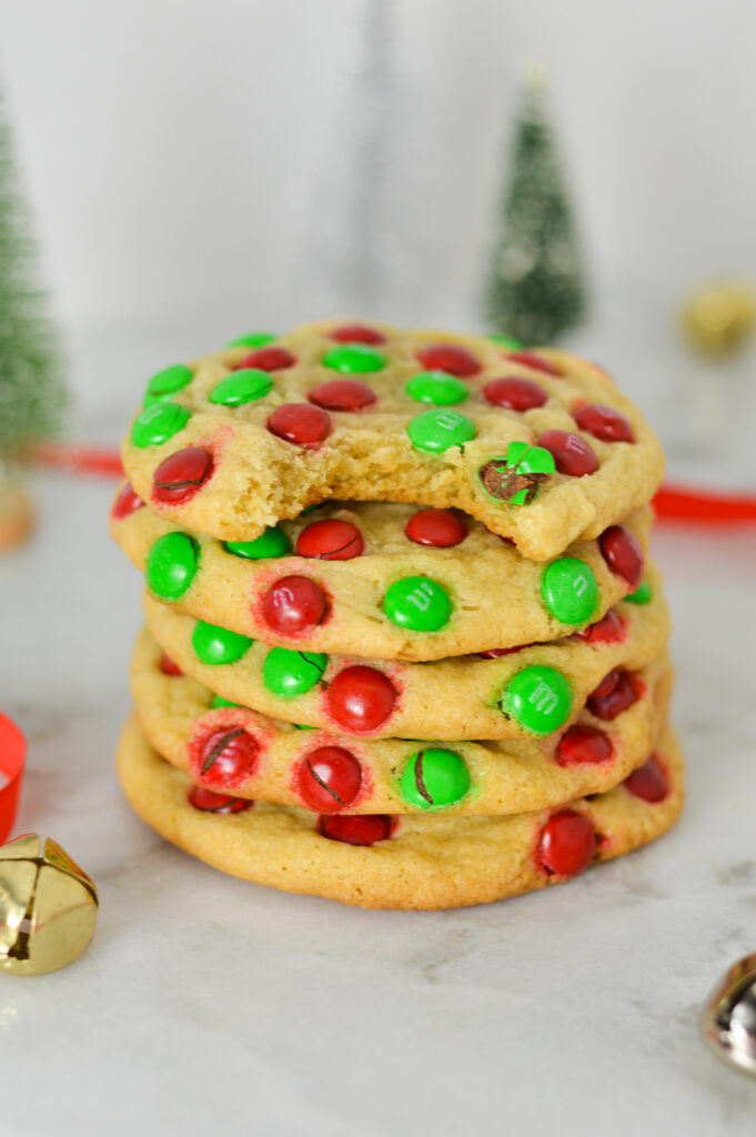 A stack of Mini M&M Christmas Cookies with a bite taken out of the top cookie, showing the chewy texture.