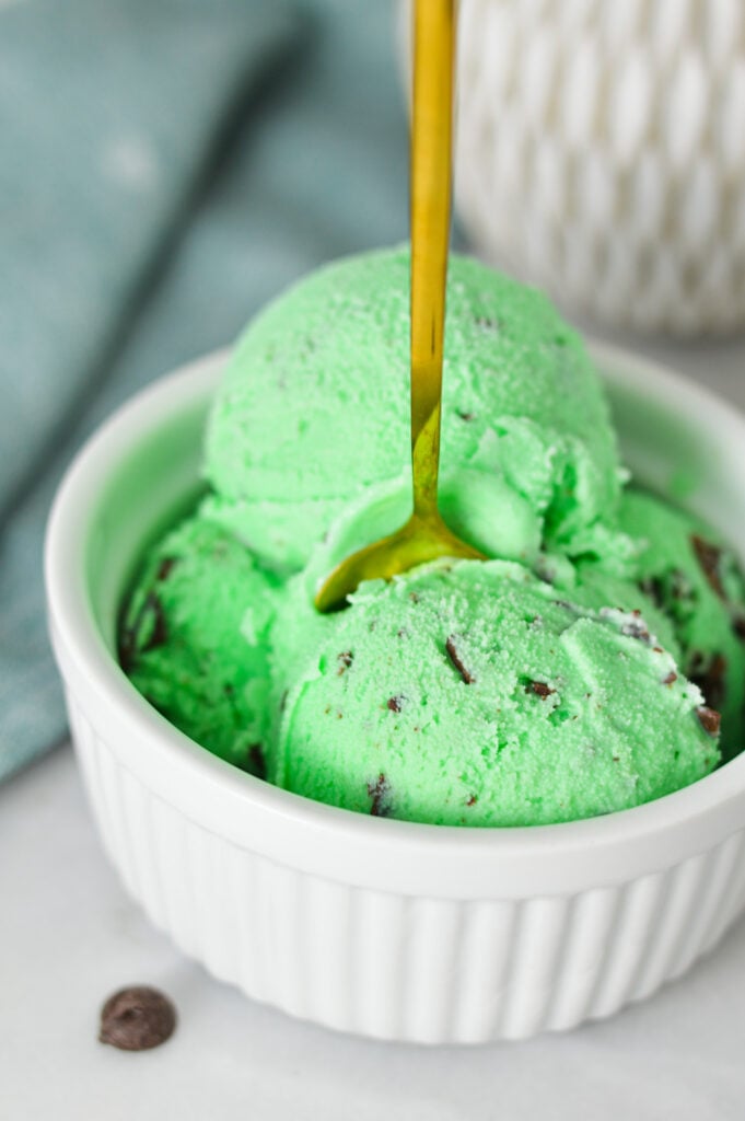 A small bowl full of scoops of Ninja Creami Mint Chocolate Chunk Ice Cream, with a golden spoon sticking out of the mint green ice cream.
