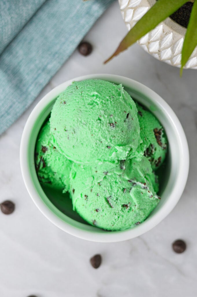 A small bowl full of scoops of Ninja Creami Mint Chocolate Chunk Ice Cream, with semi sweet chocolate chips on the granite surface beside the creamy dessert.