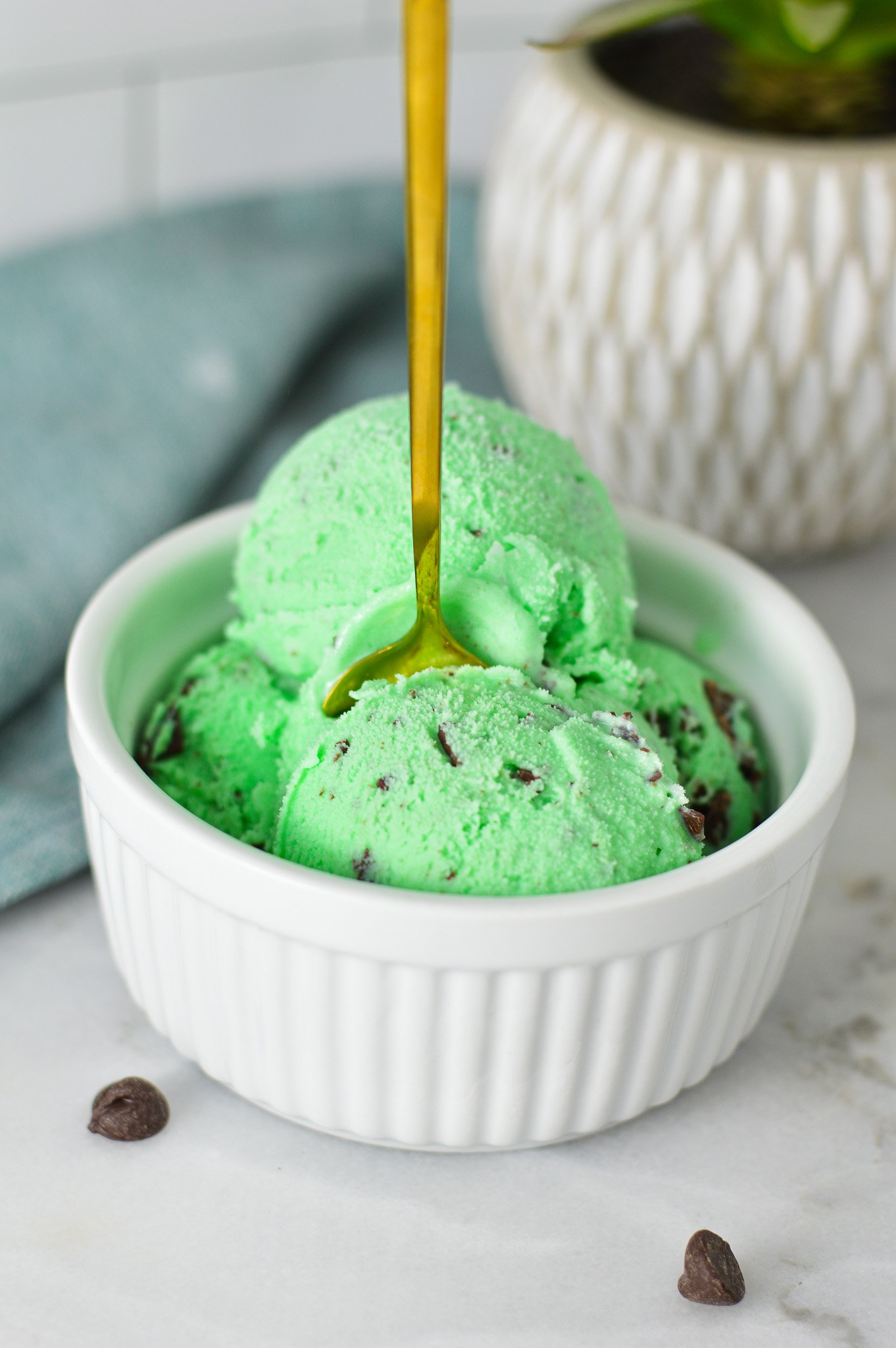 A small ramekin filled with Ninja Creami Mint Chocolate Chunk Ice Cream, with a small spoon sticking out of the mint ice cream.