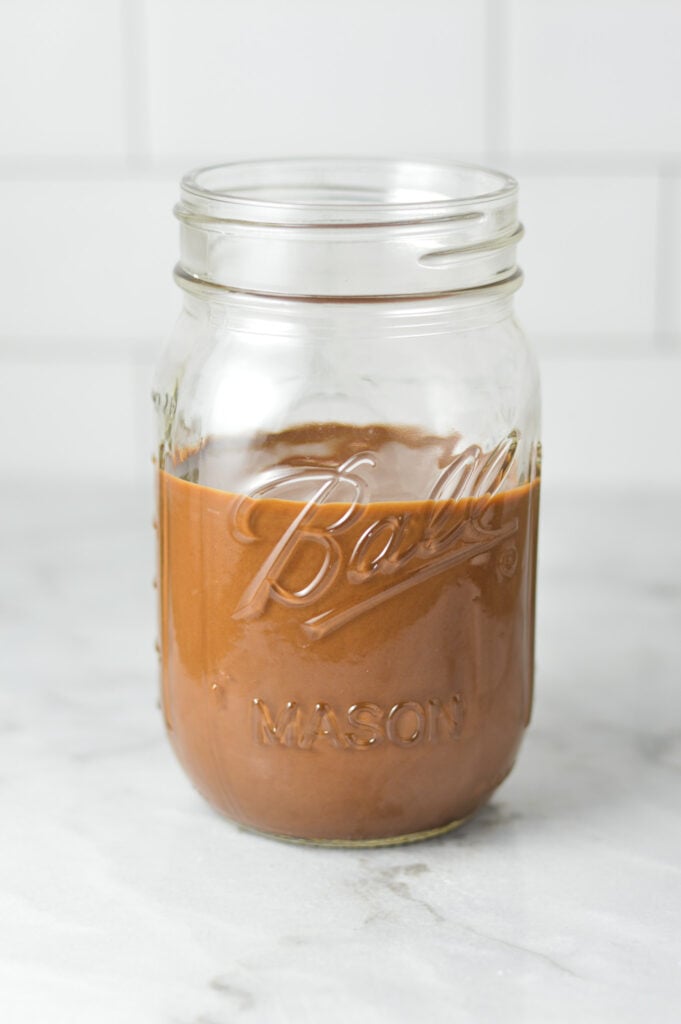 A mason jar full of liquid Nutella Magic Shell on a granite surface.